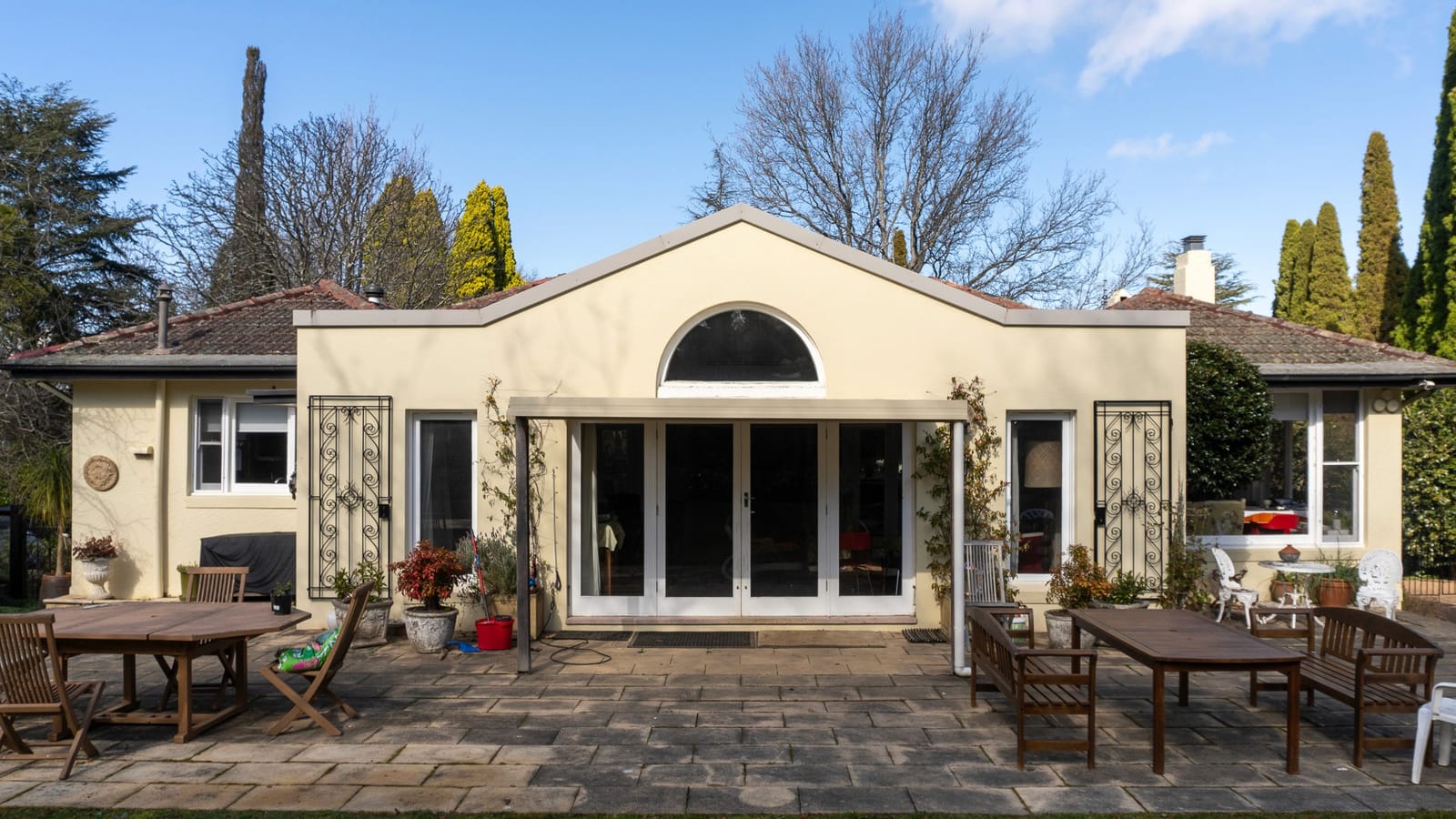 Beatrice Park in sunshine, with outdoor furniture set out on the paved terrace beneath an arched window.
